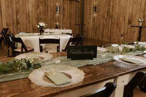 Wedding reception tables with rustic wooden decor and elegant place settings in warm lighting.