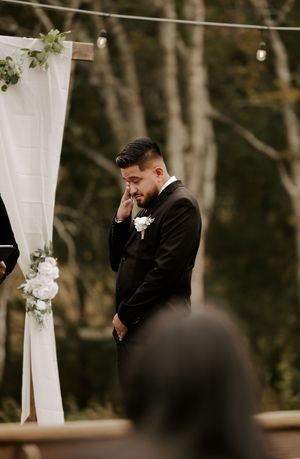 An emotional moment at a wedding ceremony under a white draped arch with floral decorations.