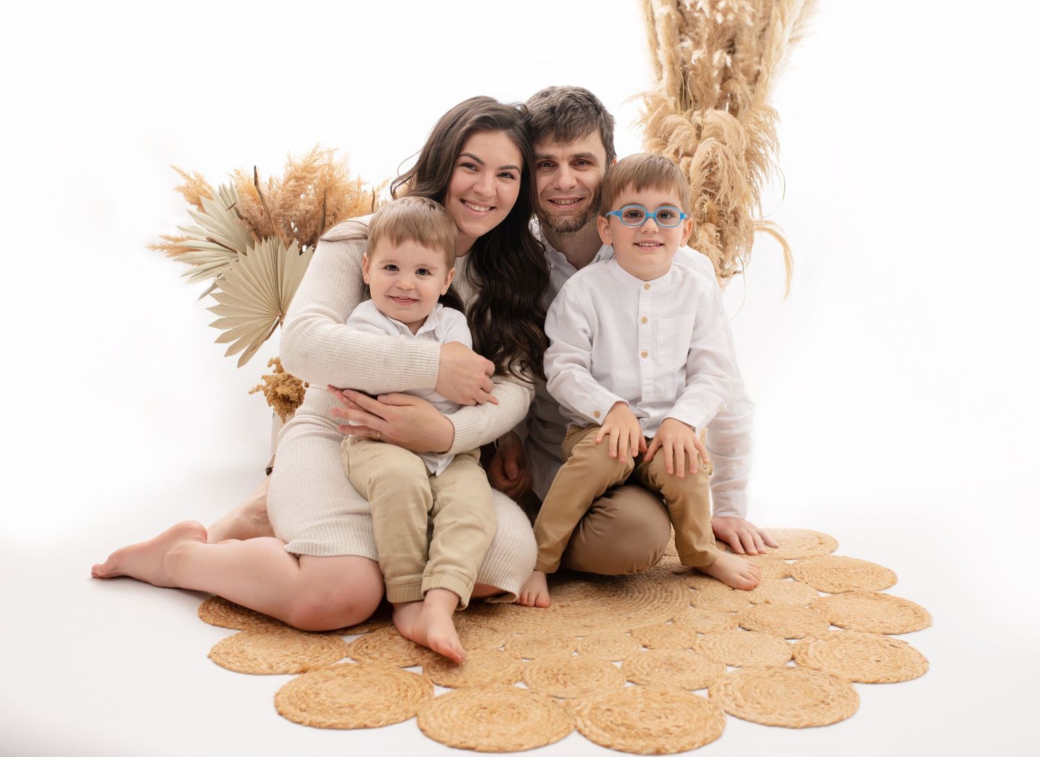 Family sitting together on circular beige rug with pampas grass decorations in neutral tones.