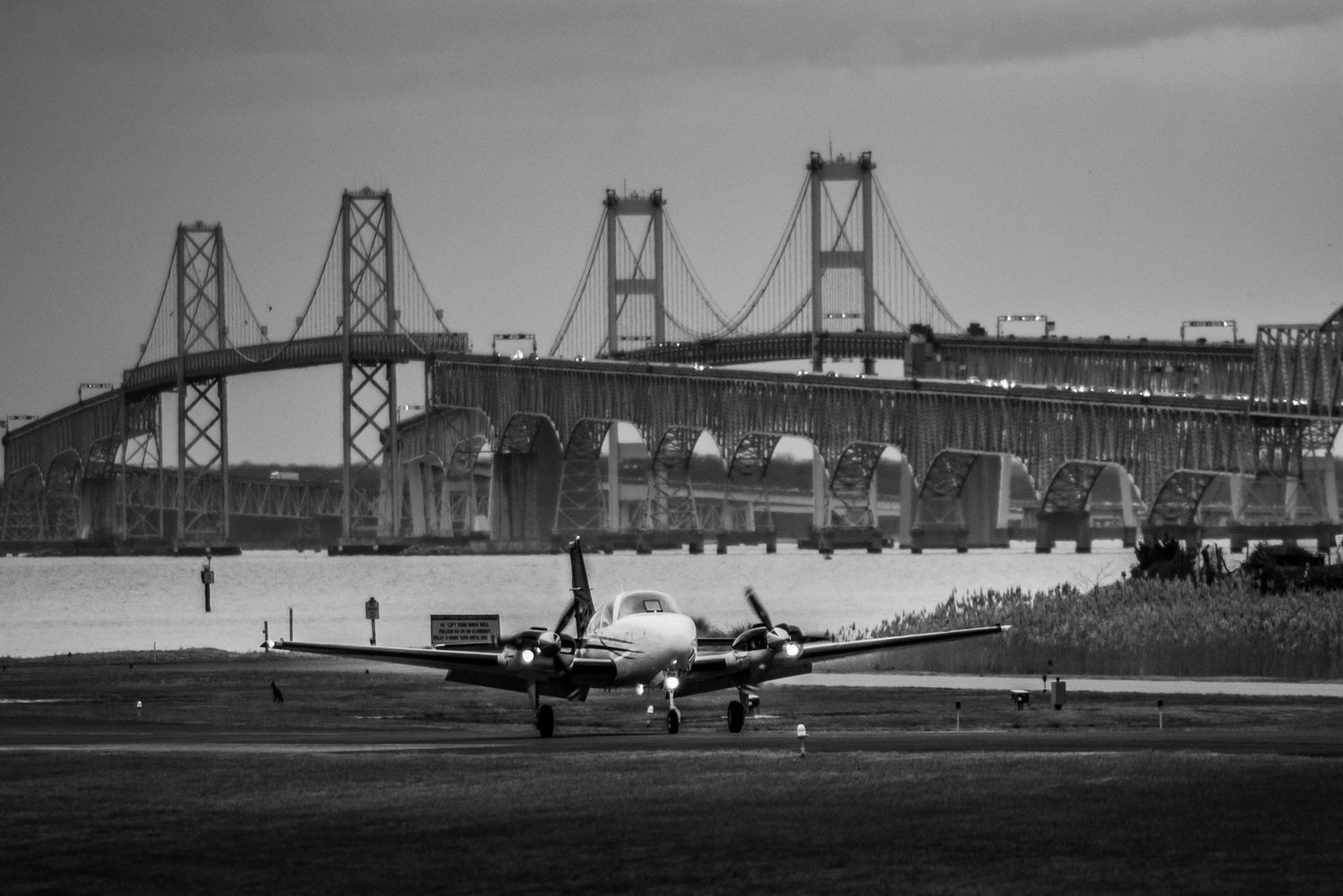 Panoramic black and white view of bridge with aircraft taking off.