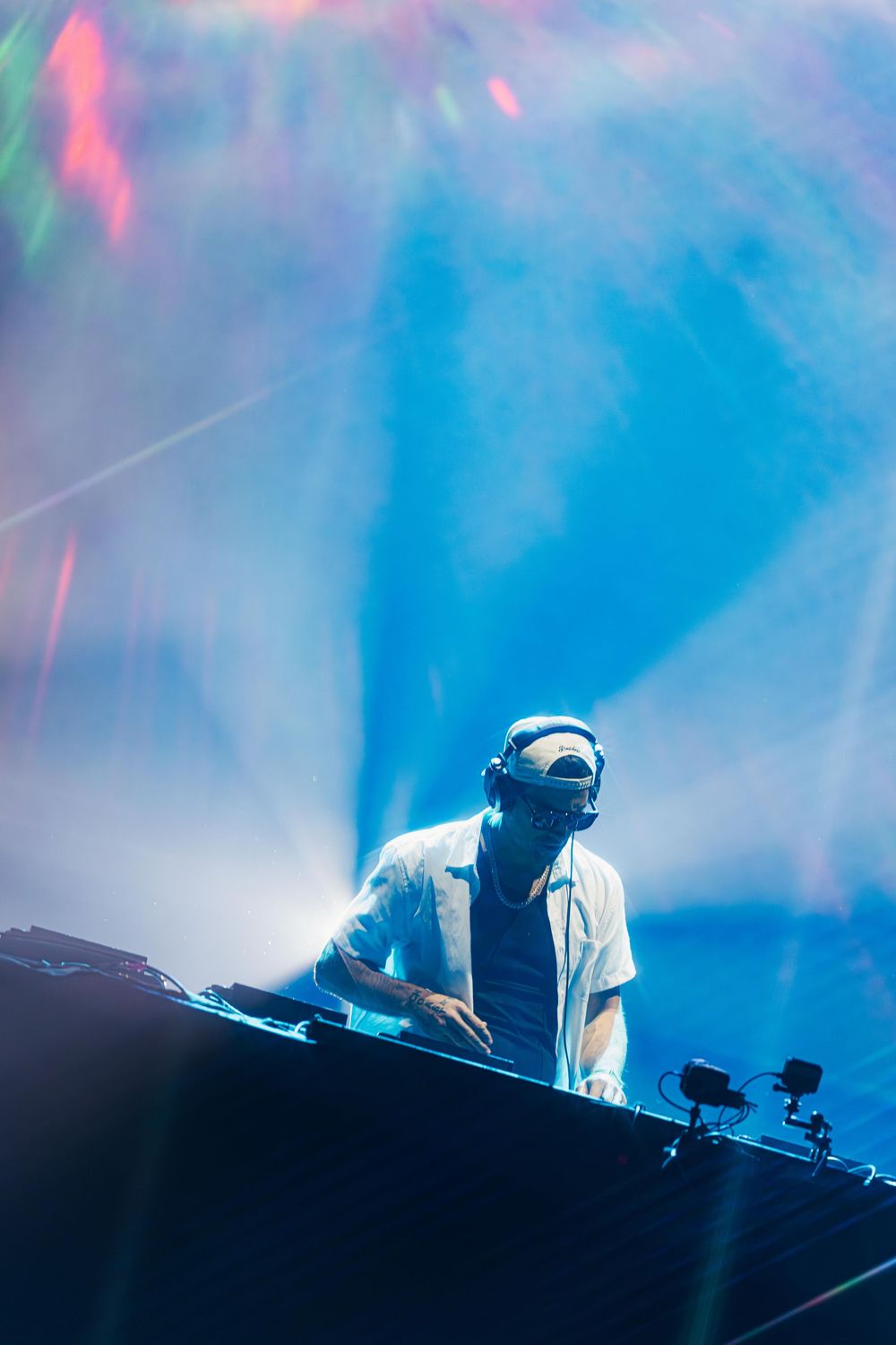 DJ performs on stage with atmospheric blue lighting and pink accents creating a moody electronic music atmosphere.