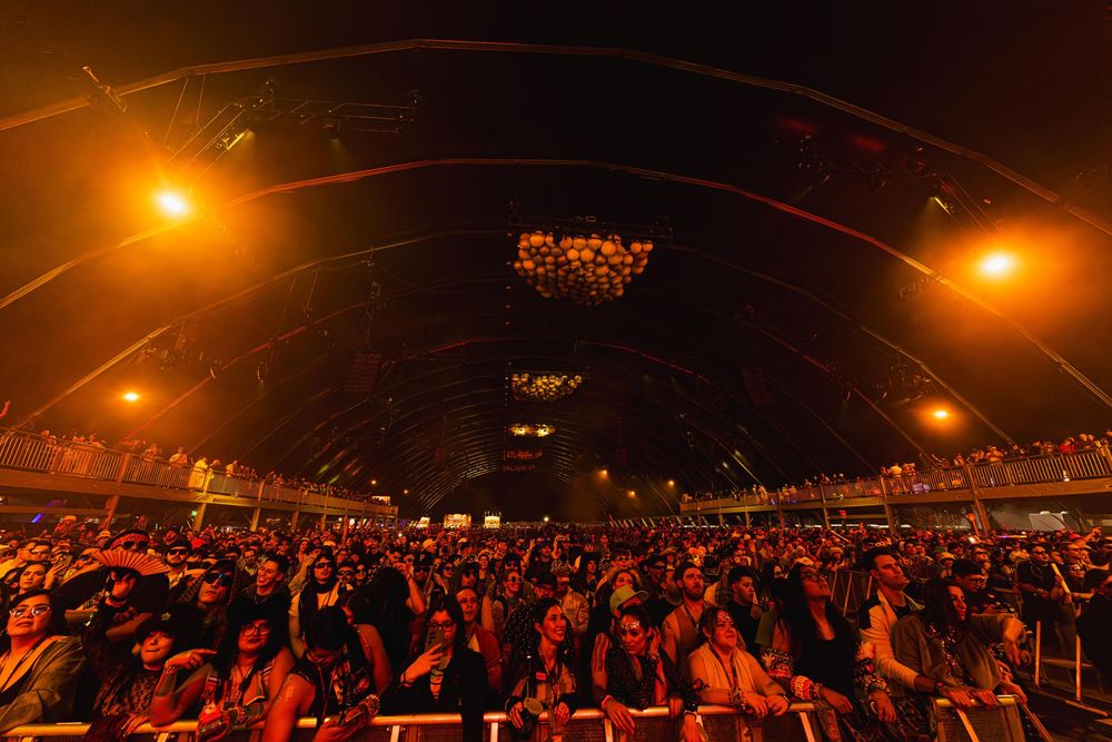 Large crowd fills an indoor arena illuminated by warm orange lighting during a nighttime event.