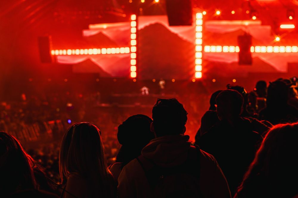 Concert crowd silhouettes against bright red stage lighting and smoke effects during a live performance.