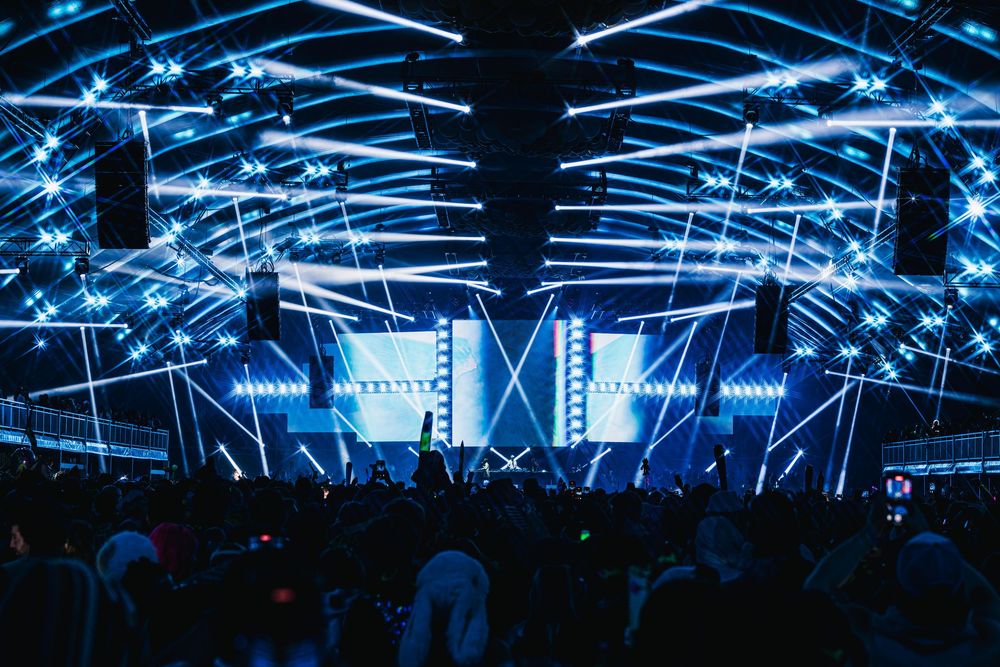 Concert venue illuminated with dramatic blue lighting and laser beams creating an atmospheric nightclub environment.
