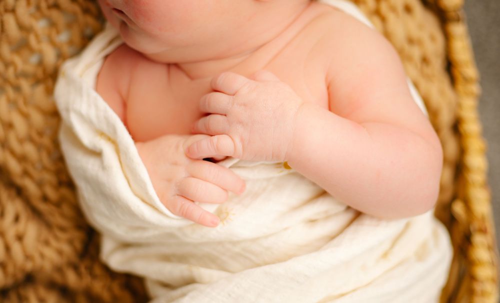 Newborn baby feet wrapped in cream blanket on woven basket.