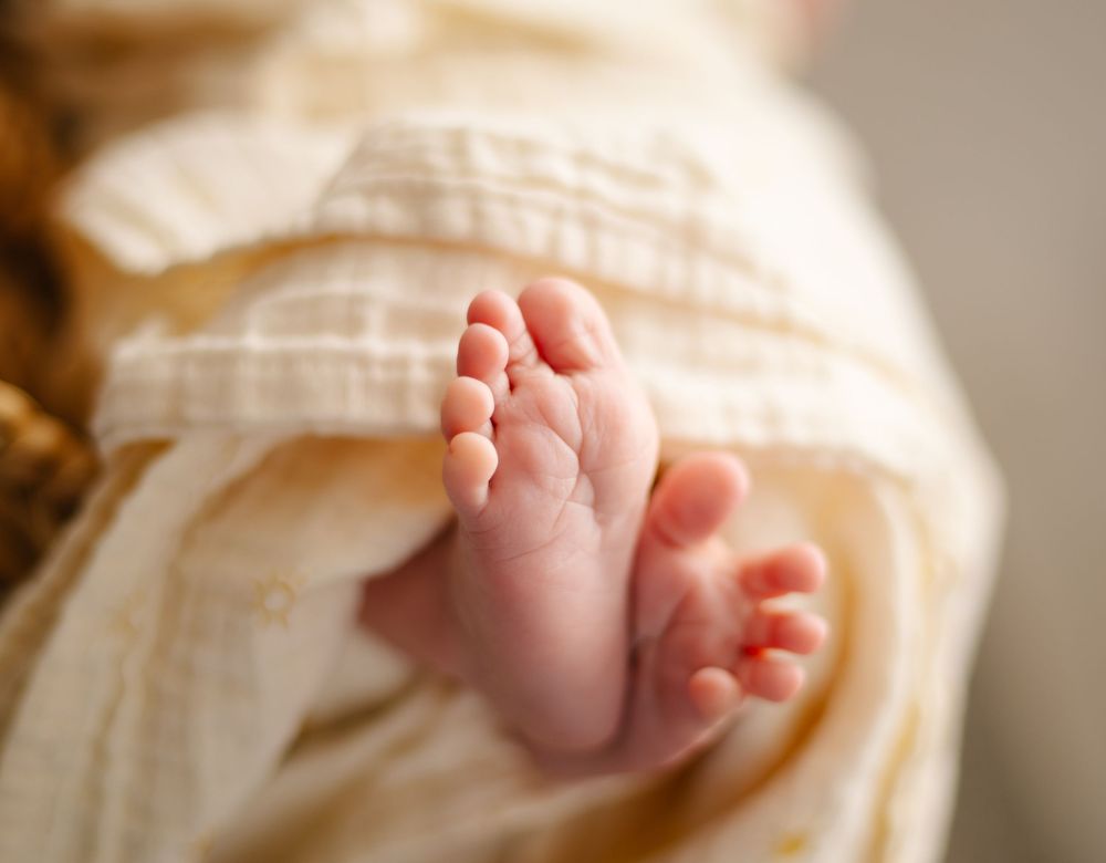 Close-up of tiny baby feet wrapped in soft cream-colored blanket.
