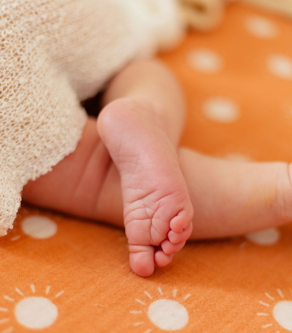 Newborn baby toes on orange spotted fabric with white blanket.