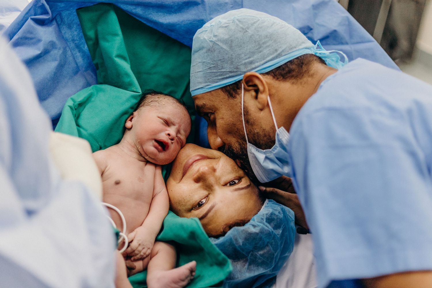 Medical team in blue scrubs and surgical caps performing a cesarean section delivery in an operating room.