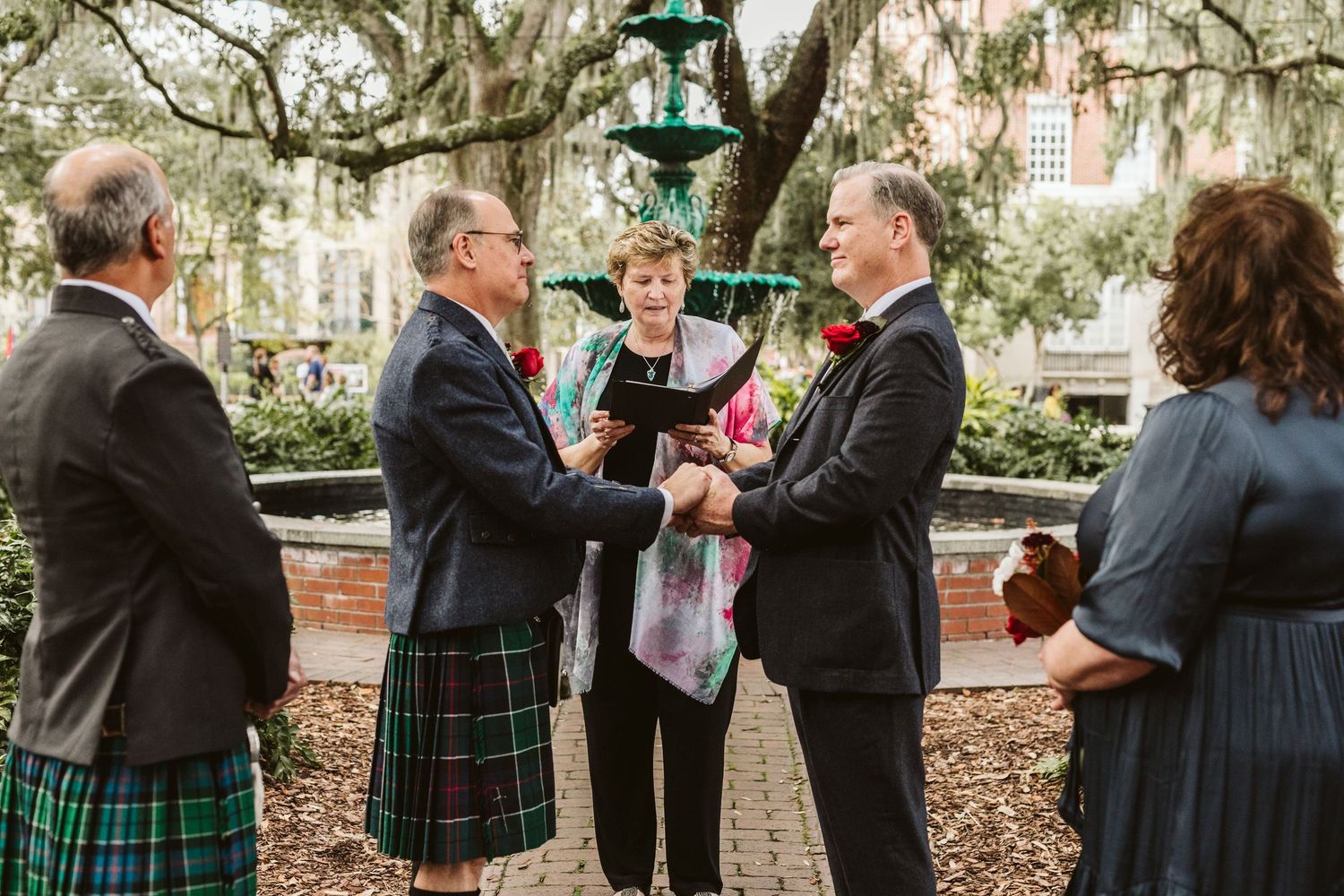 Outdoor wedding ceremony in a garden setting with guests gathered under oak trees draped in Spanish moss.