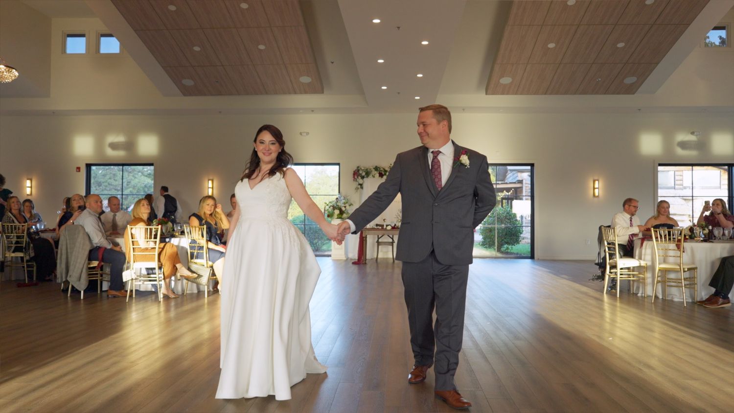 Wedding guests dance and celebrate on a large wooden dance floor in an elegant reception venue.
