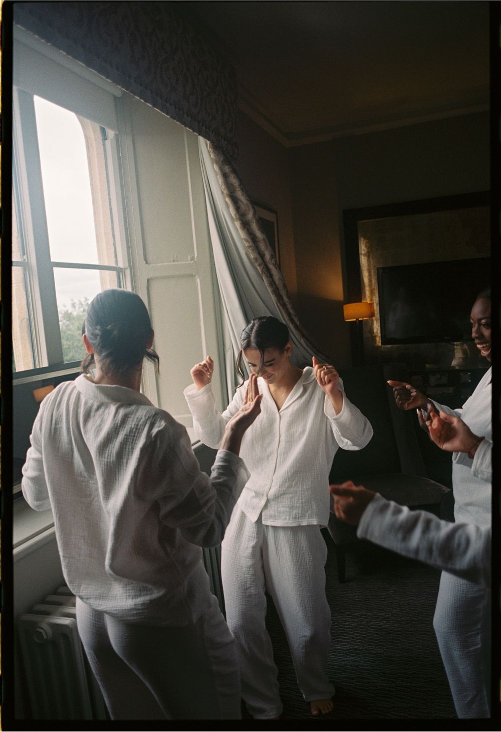People in white clothing dancing and enjoying themselves in a sunlit room.