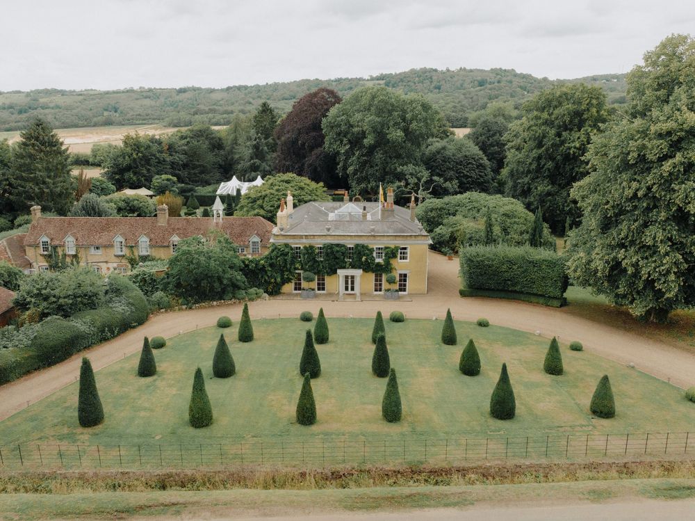 Panoramic view of a manicured garden with symmetrical topiary trees and estate buildings.
