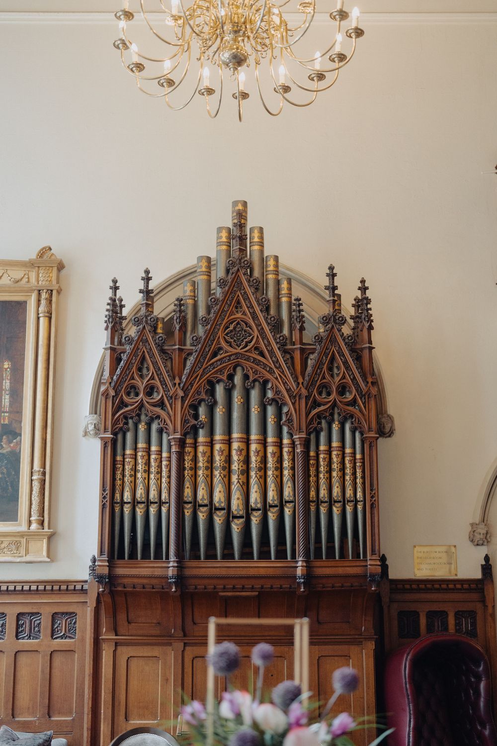 Ornate Gothic church organ pipes with intricate woodwork and chandelier overhead.