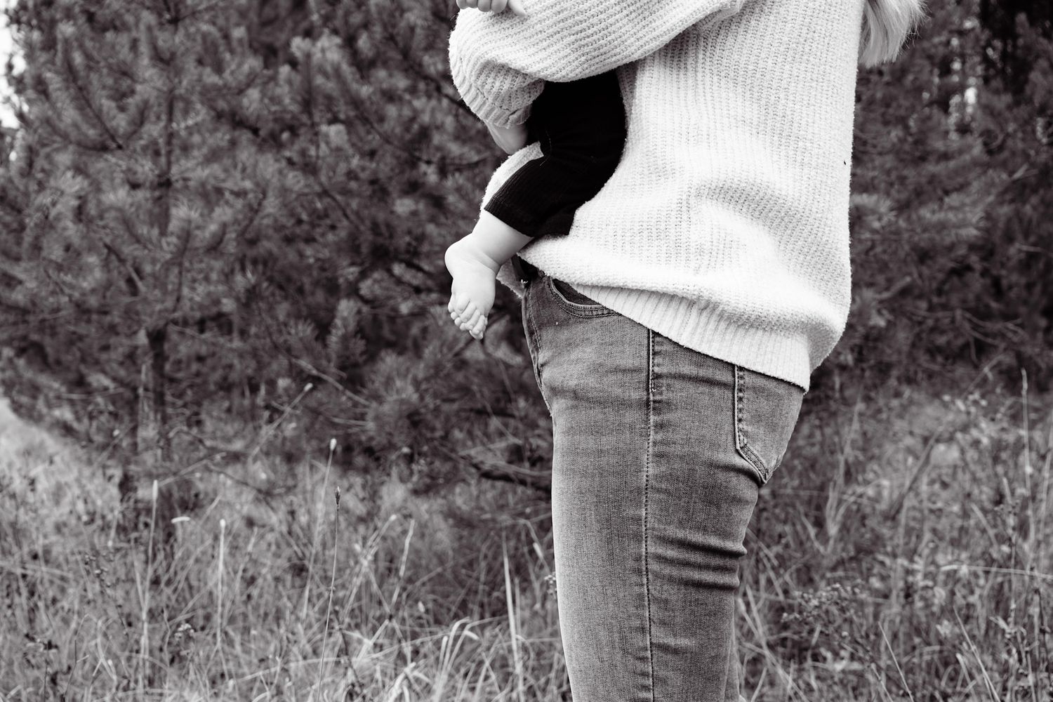 Black and white photo of legs in jeans and boots walking through tall grass.