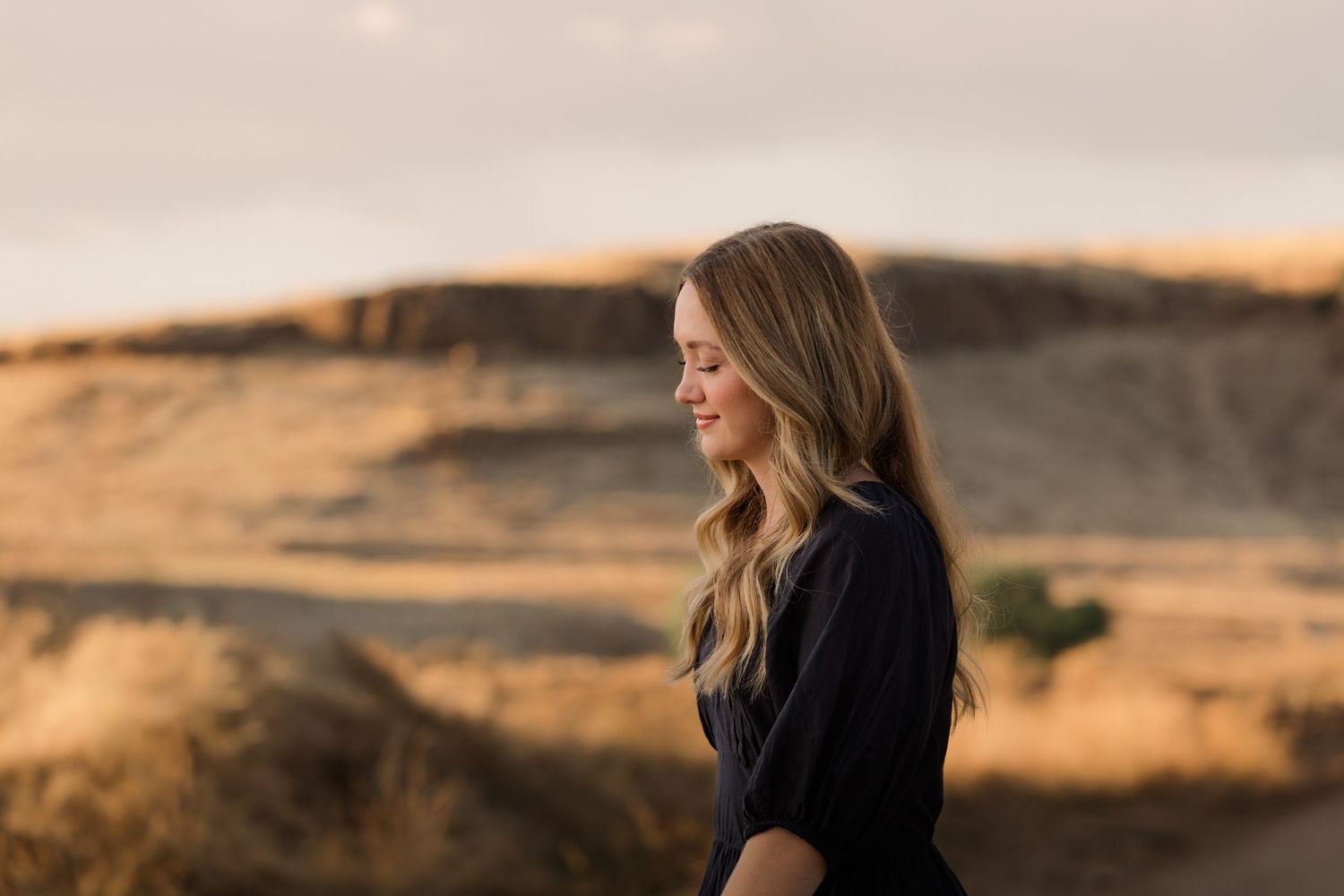 Woman in black sweater gazes at scenic desert landscape during golden hour sunset.