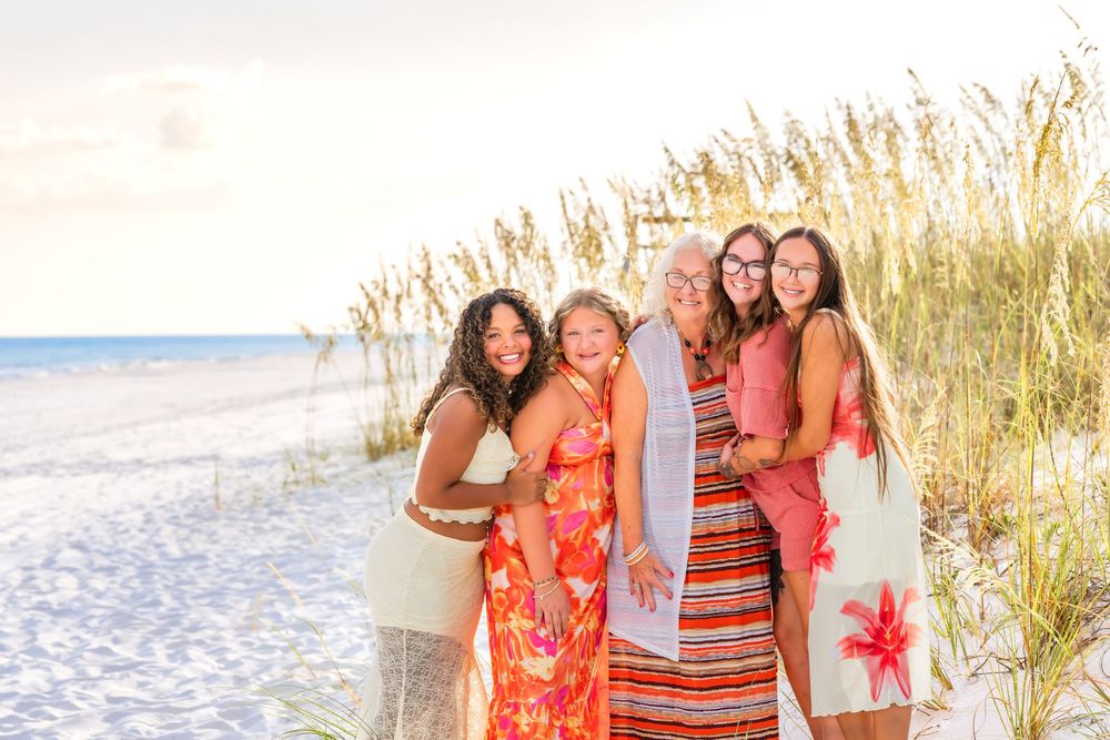 Friends gathered on a pristine beach with tall grass and bright coral-colored outfits against the ocean backdrop.