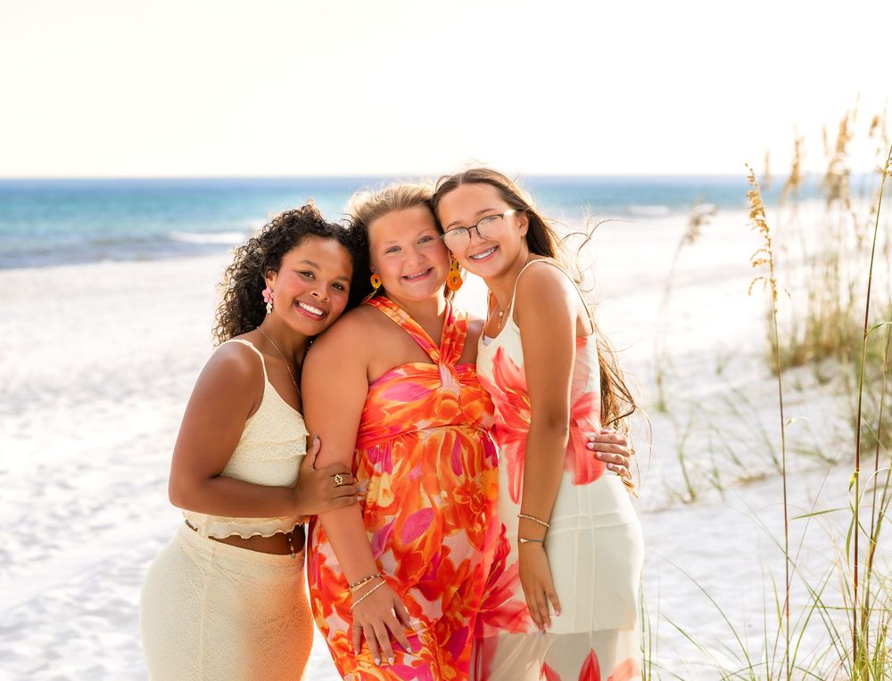 Group enjoying a sunny day together at a white sand beach with sea oats and ocean waves in the background.
