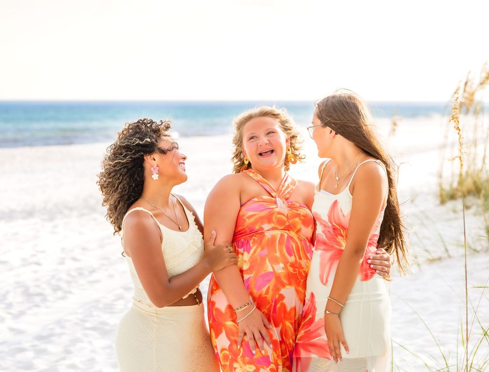 Three friends laugh together while enjoying sunset photoshoot on pristine beach.