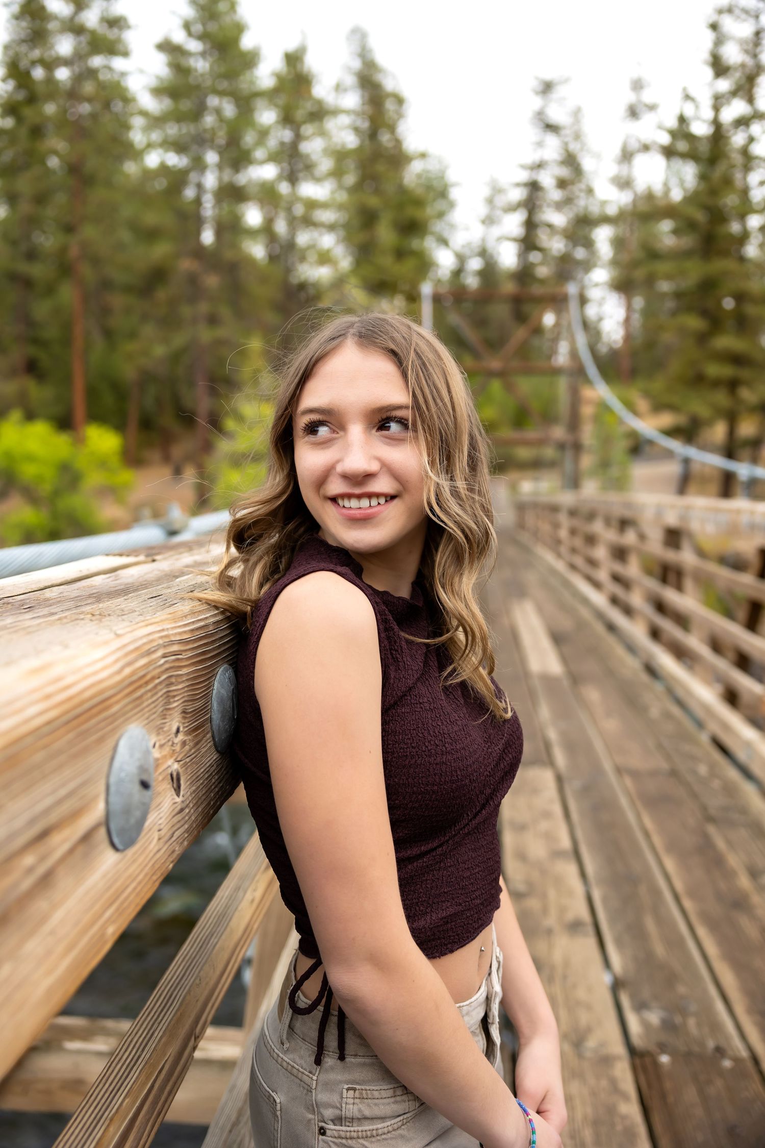 A portrait taken on a wooden boardwalk surrounded by evergreen trees on a sunny day.