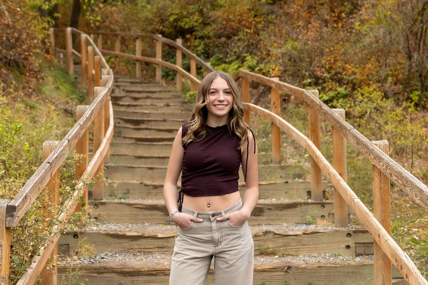 A person walks down stone steps with wooden handrails surrounded by autumn foliage in a park setting.