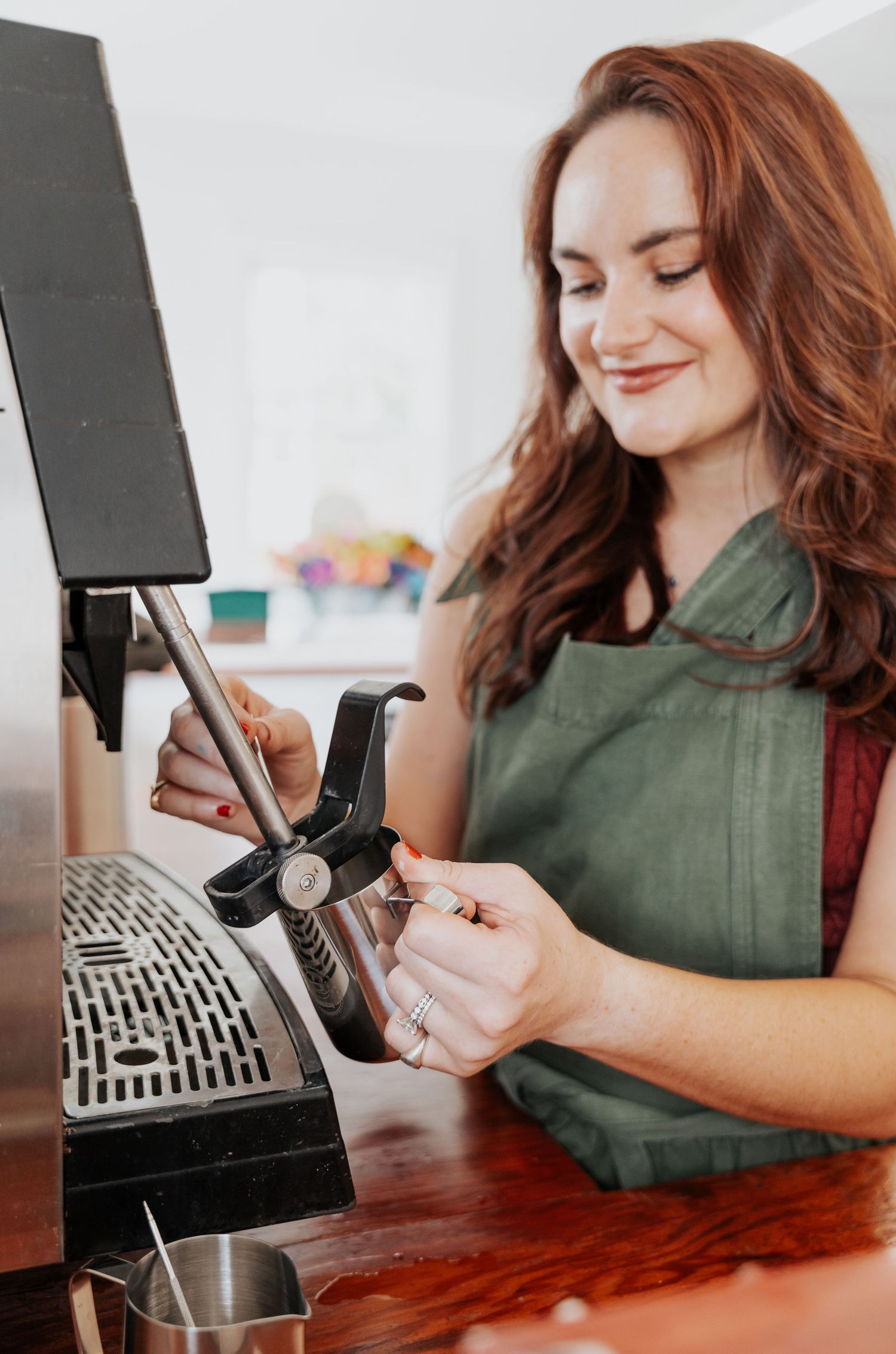 Woman in green top smiles while using vintage cash register and smartphone.
