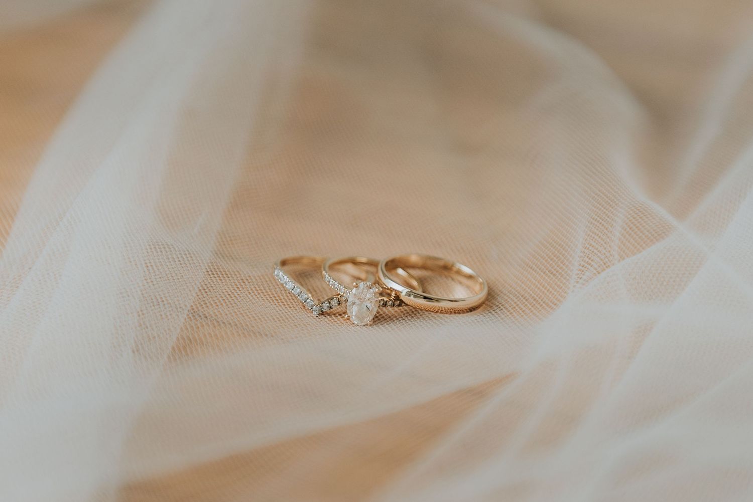Close up detail of delicate gold wedding rings resting on soft white tulle fabric in natural light.