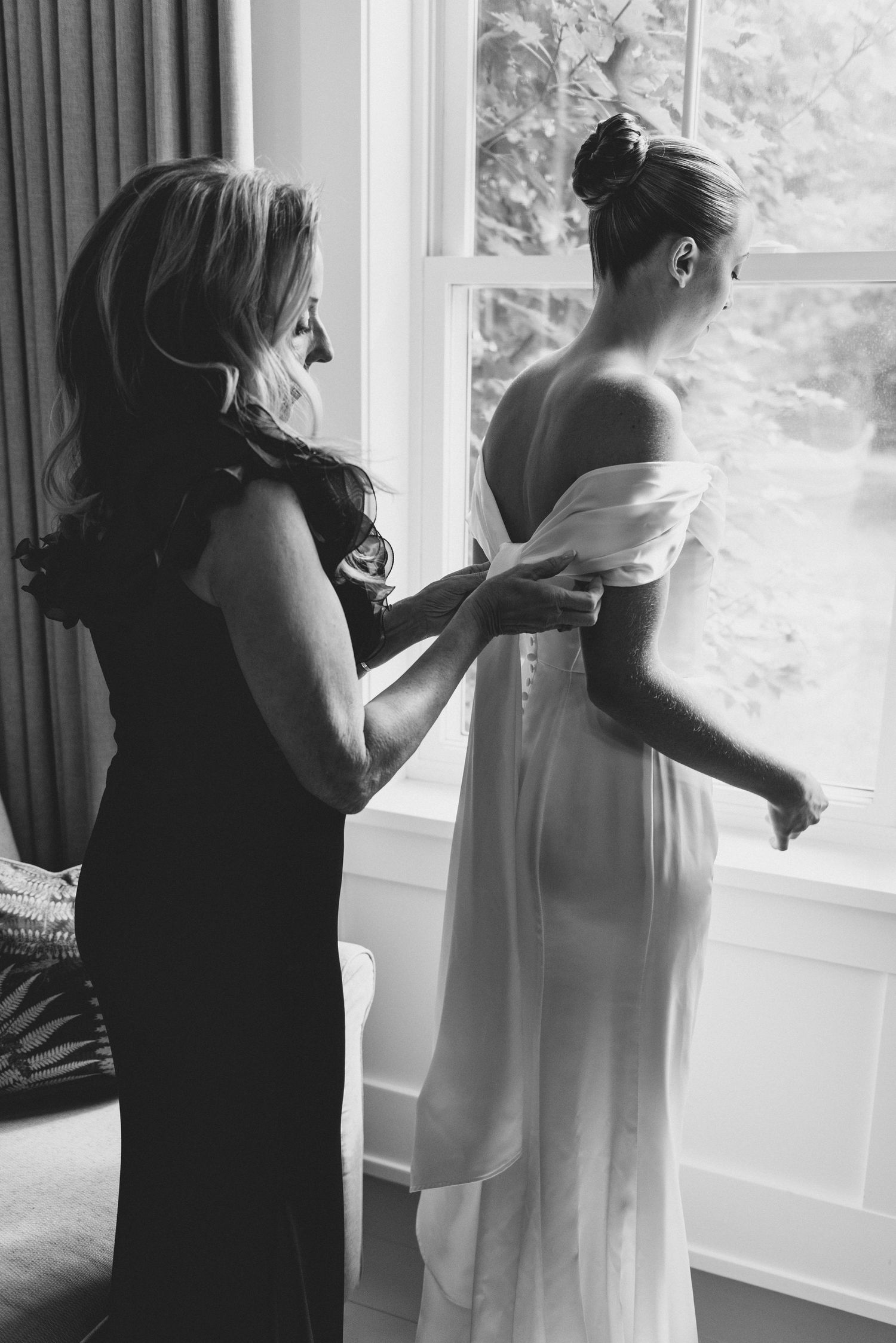 Black and white photo series showing figures in formal attire getting ready by a window in a bridal preparation scene.