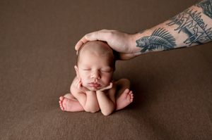 A sleeping newborn baby lies on a brown blanket with hands and feet visible in a professional portrait setting.