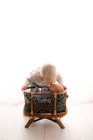 A child peers into a rustic rattan chair with cushions against a bright white background.