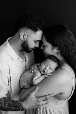 A tender black and white portrait of parents embracing their sleeping newborn baby in an intimate family moment.