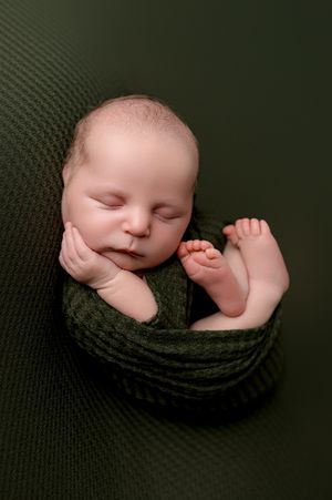 A sleeping baby nestled in a cozy black knit wrap against a dark background.
