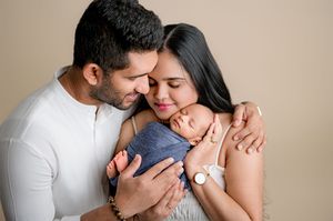 A couple tenderly holds their swaddled newborn baby during a professional studio newborn photography session.