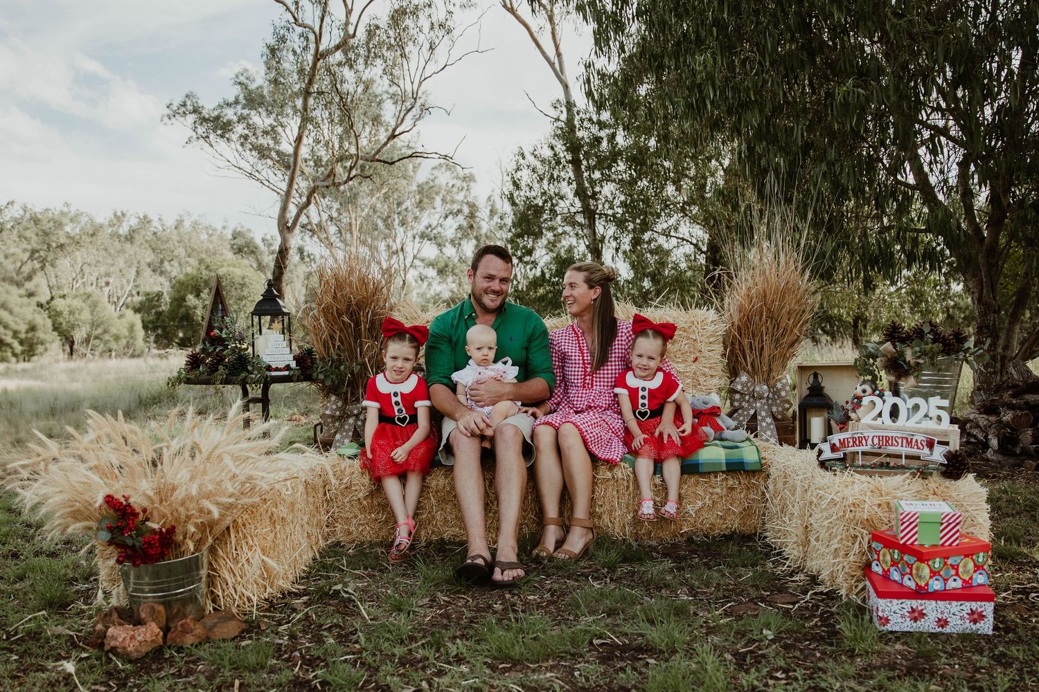 Mother looking at father while sitting on hay bales with their 3 girls for a professional christmas mini photo shoot