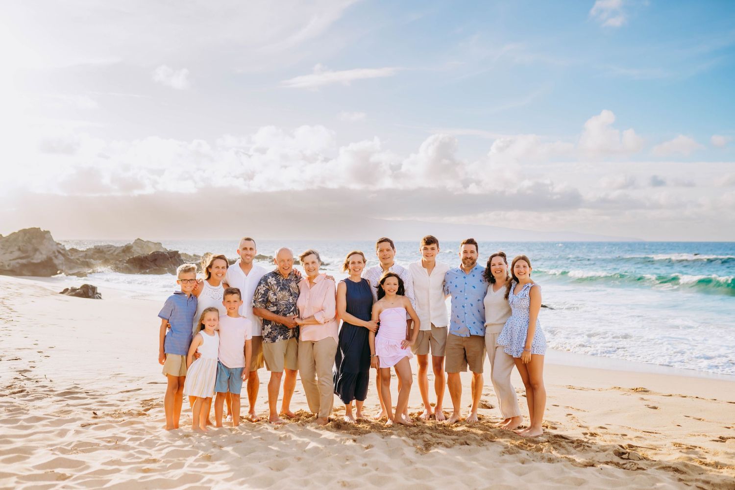 Extended family group in coordinated beach attire poses together on sandy shoreline.