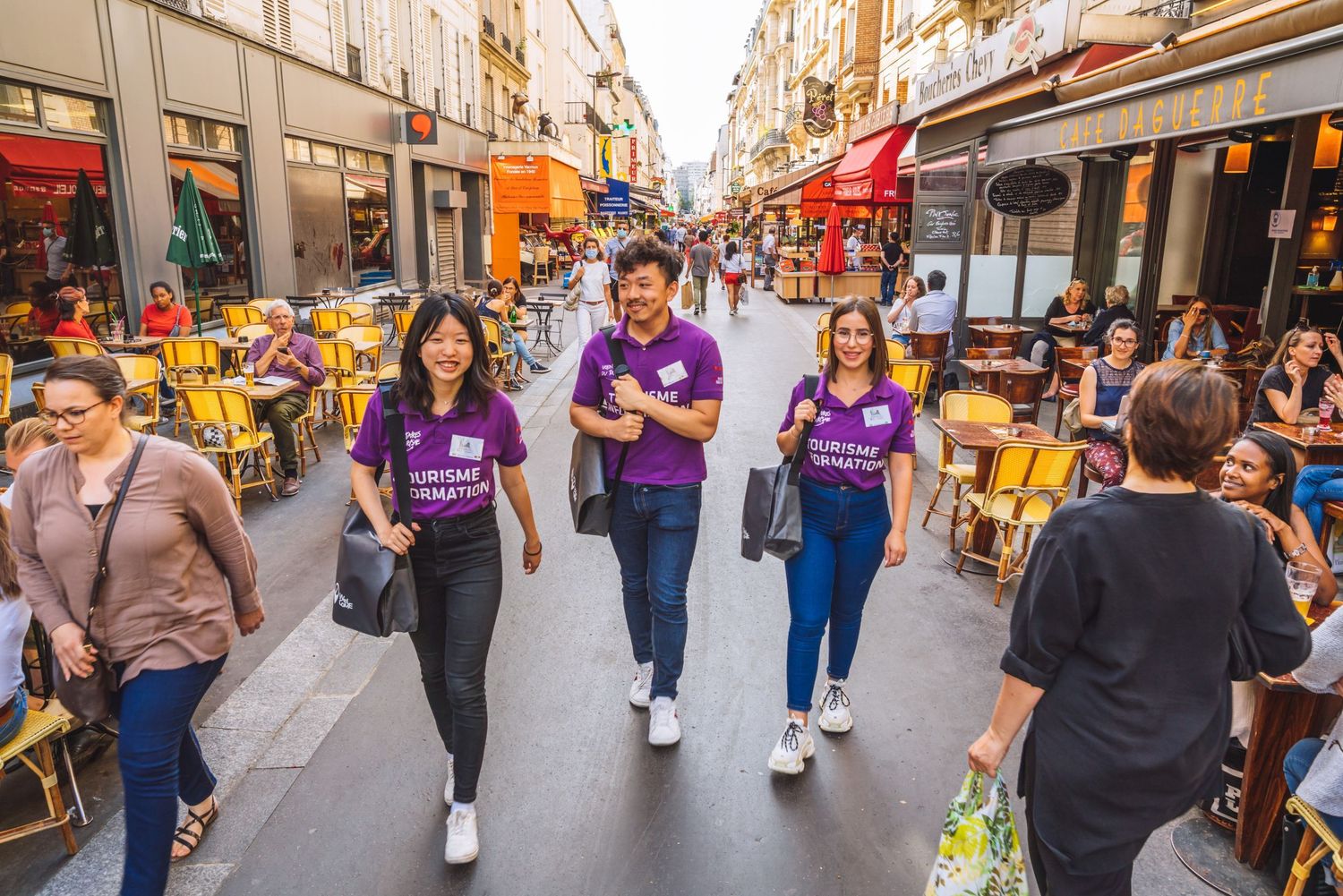 Busy pedestrian street in Paris with restaurants, cafes and people walking along the cobblestone path on a sunny day.