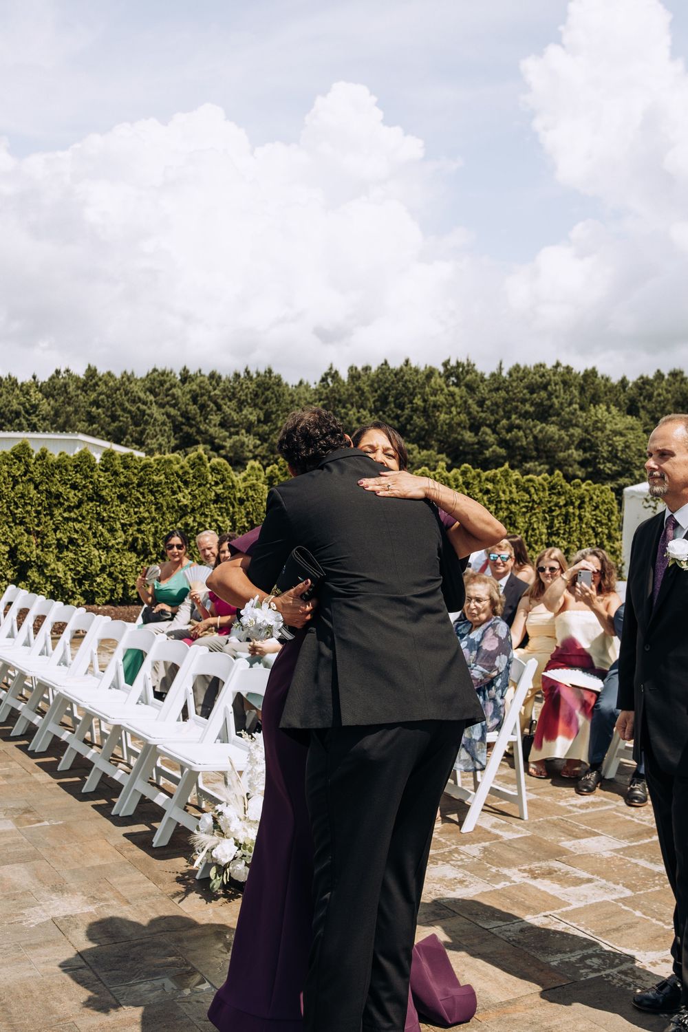 Groom shares emotional hug with mother at outdoor wedding ceremony aisle.