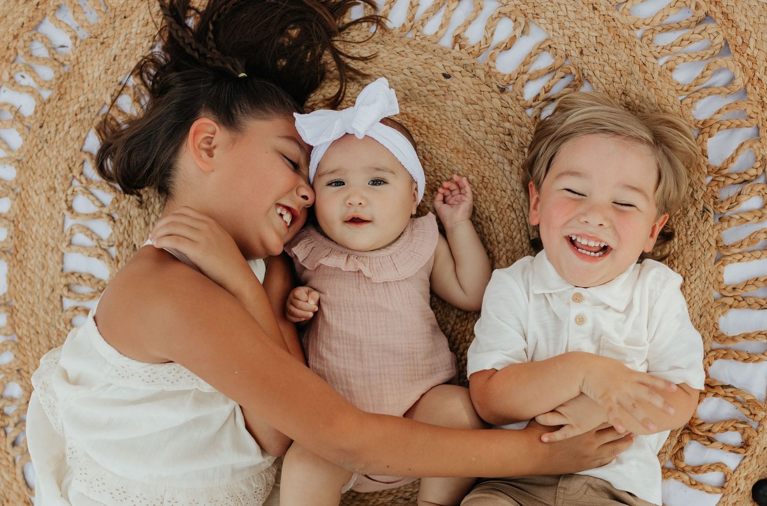 Lifestyle family portrait of siblings cuddling together on a textured blanket in warm natural light.