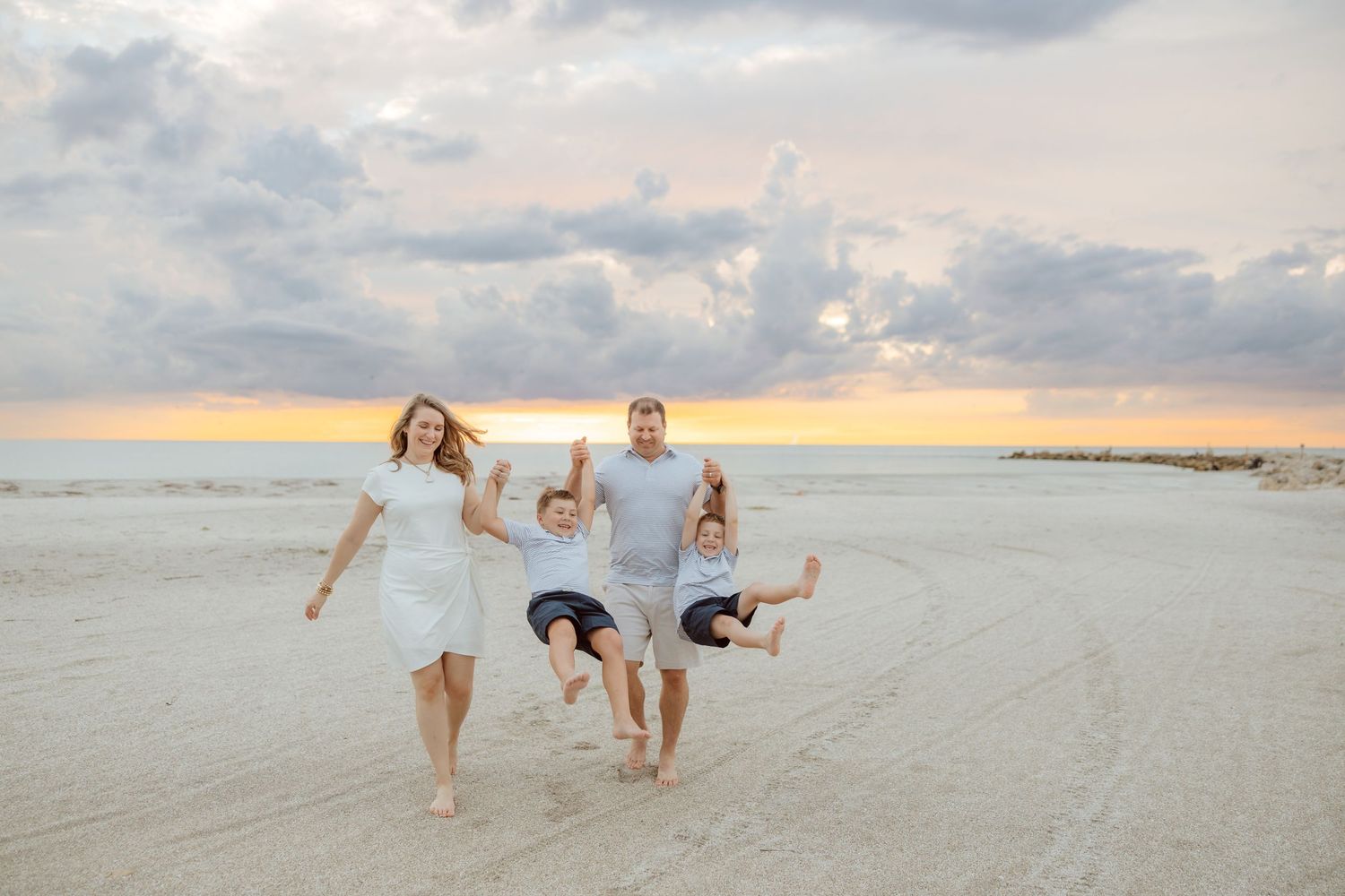 Lifestyle family photo of a parent lifting their child near the shoreline during a playful beach session.