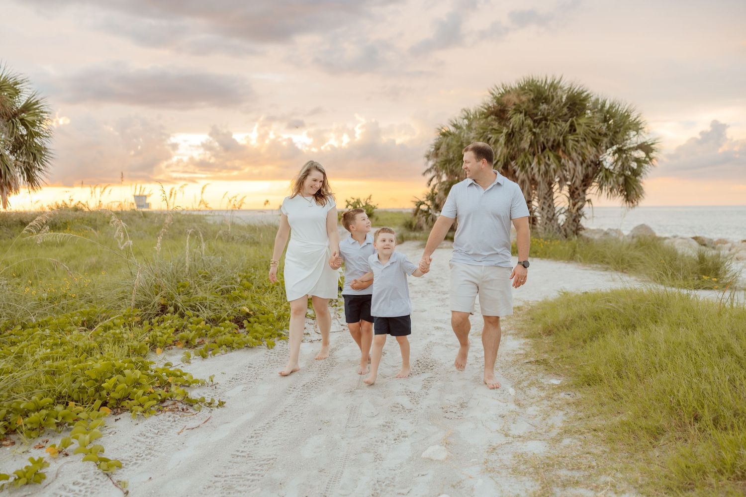 Beach family portrait of parents and children walking together along a sandy path at sunset.