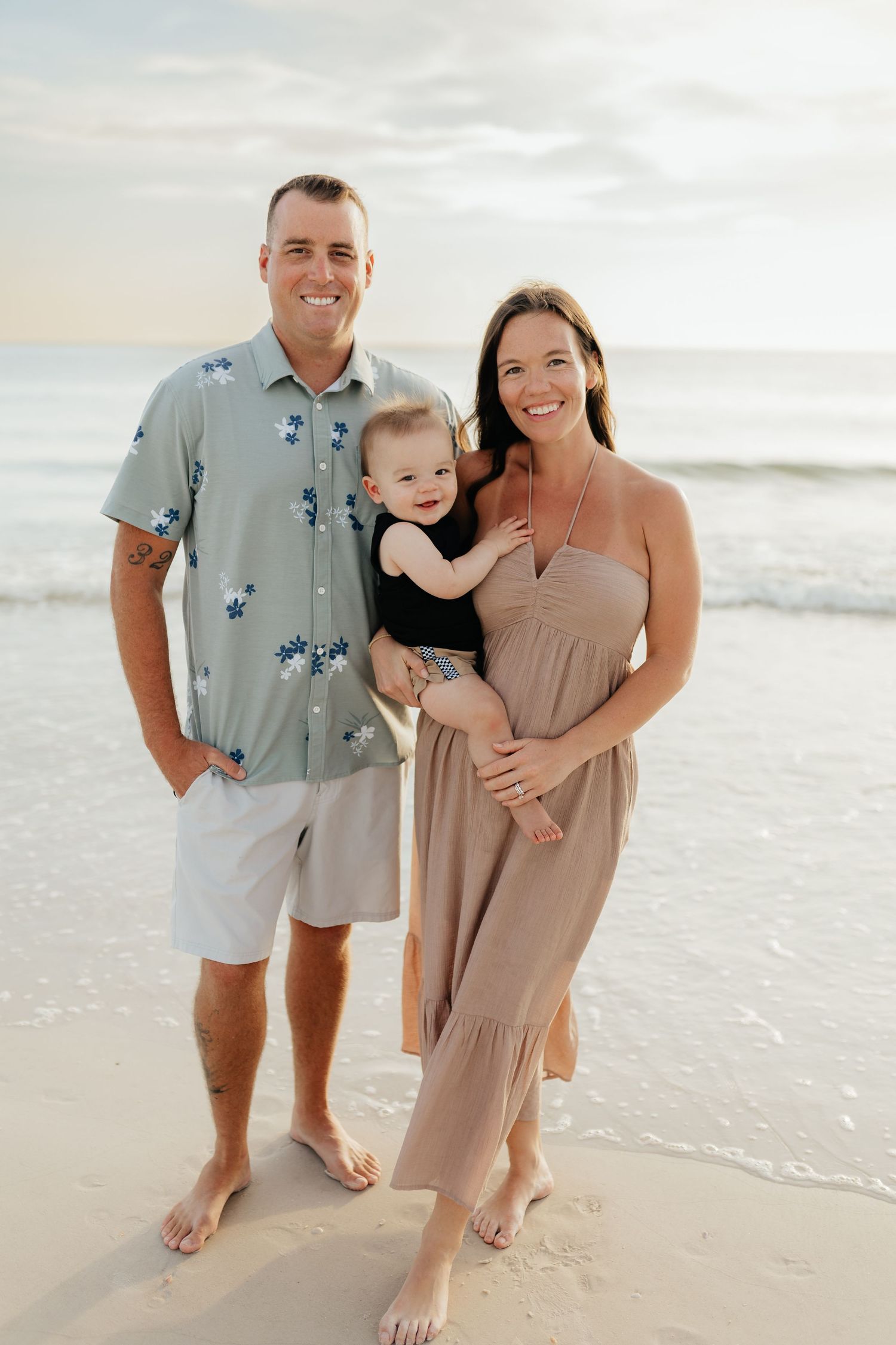 Beach family portrait of parents standing together with their child during a relaxed lifestyle session.