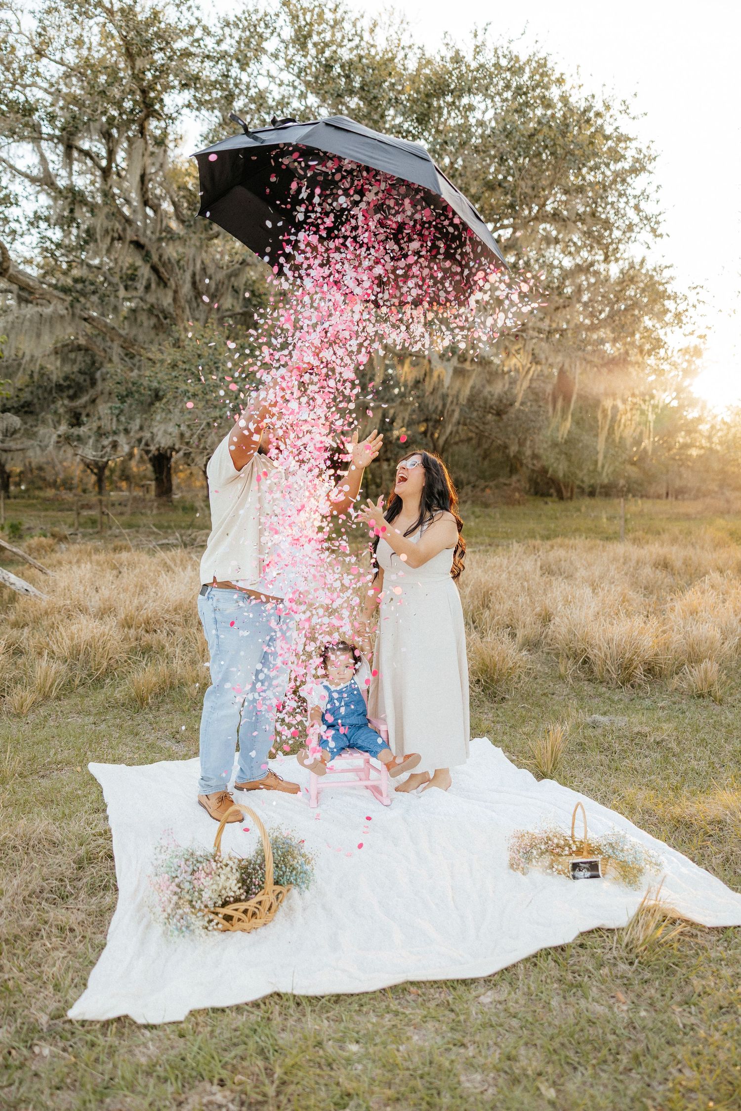 Lifestyle family photography capturing a joyful gender reveal moment with confetti during an outdoor session.