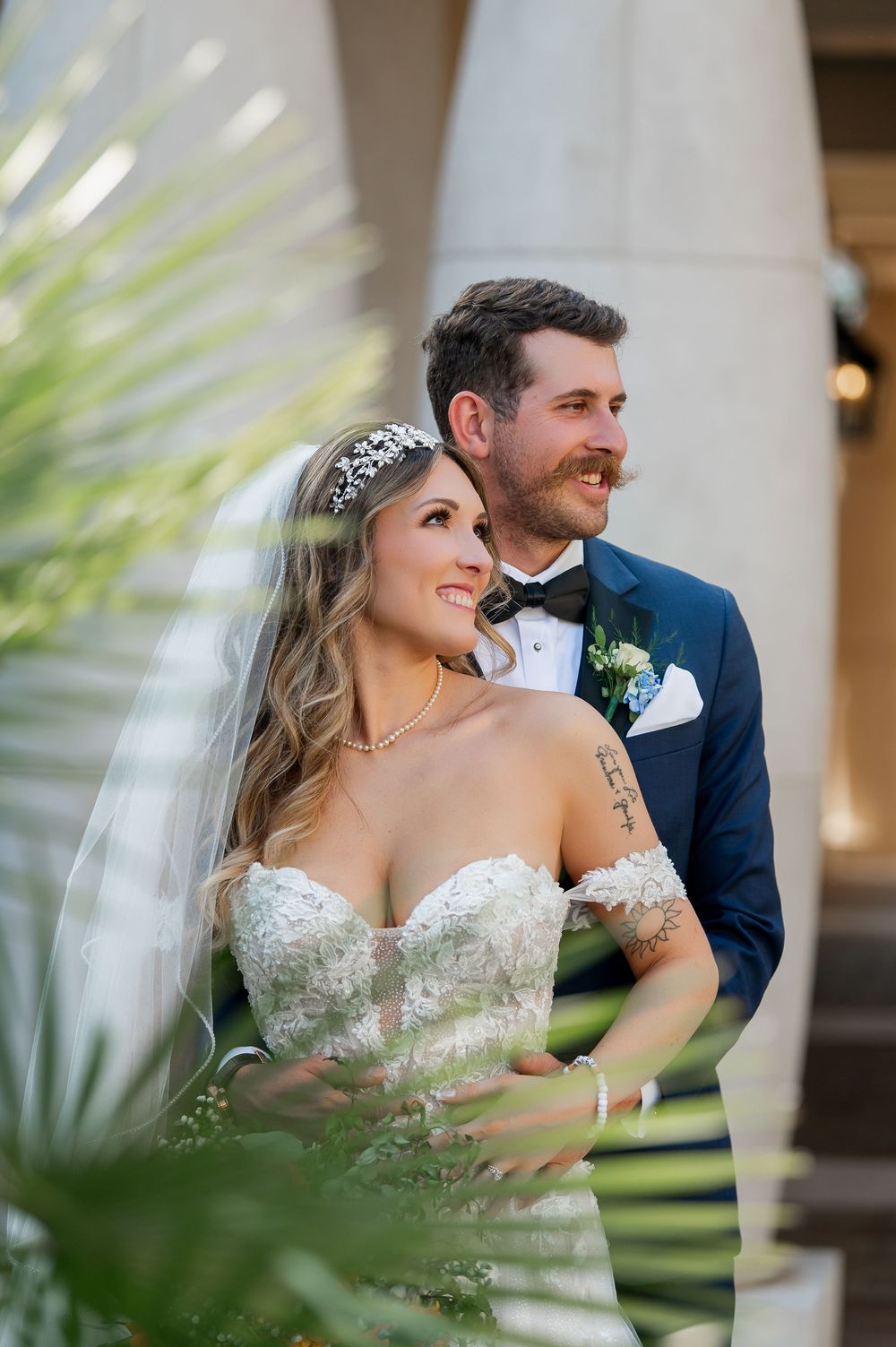 A joyful wedding couple poses together among palm fronds at their elegant venue.