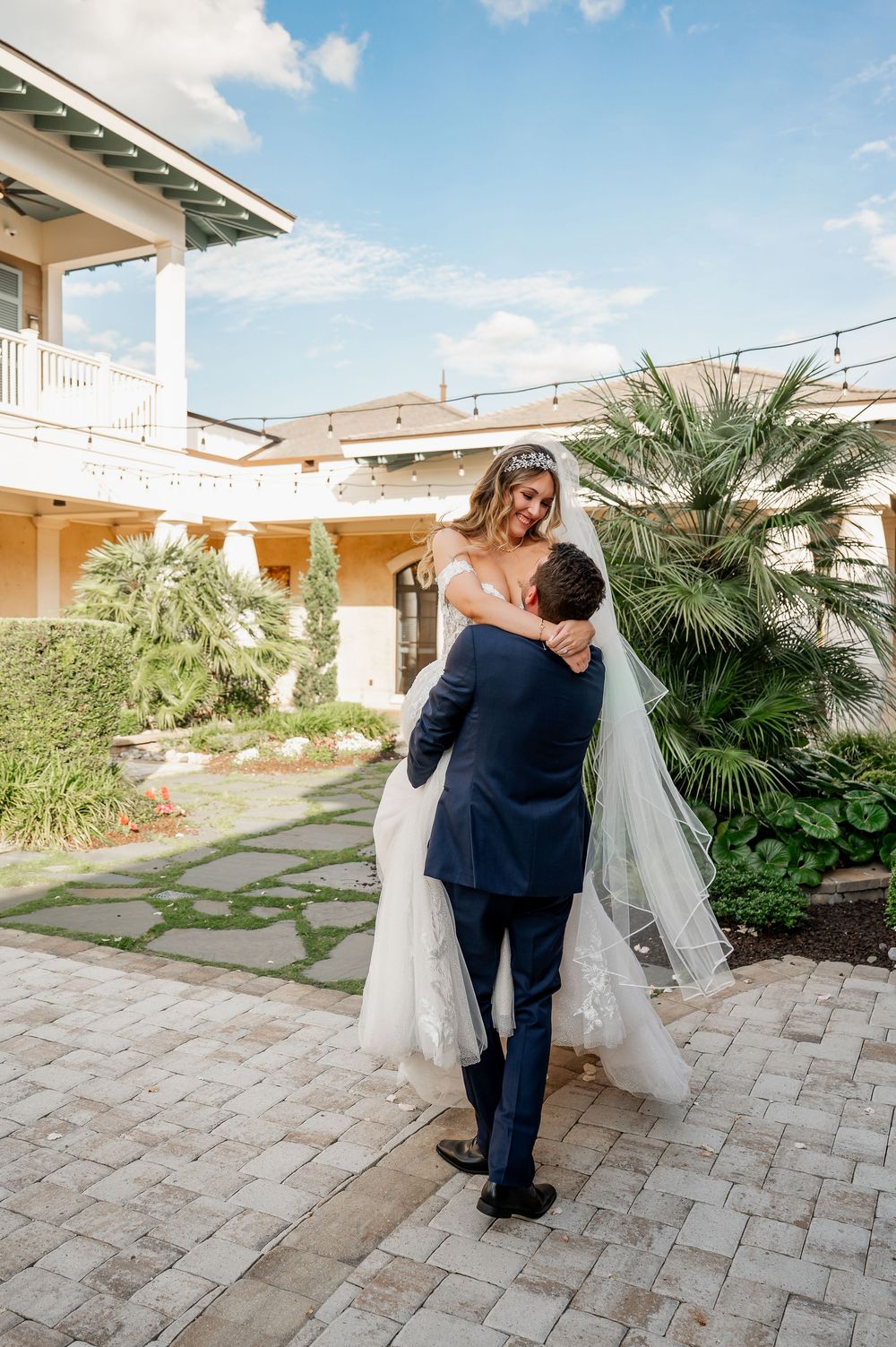 A playful wedding moment captured as the groom lifts his bride at an elegant outdoor venue.