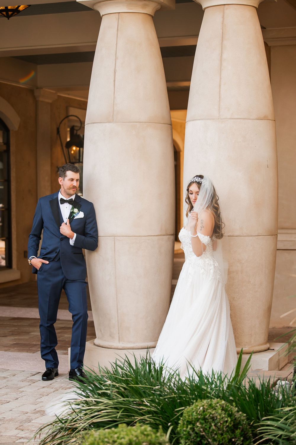 A creative wedding portrait with the couple posing playfully on opposite sides of elegant stone columns.