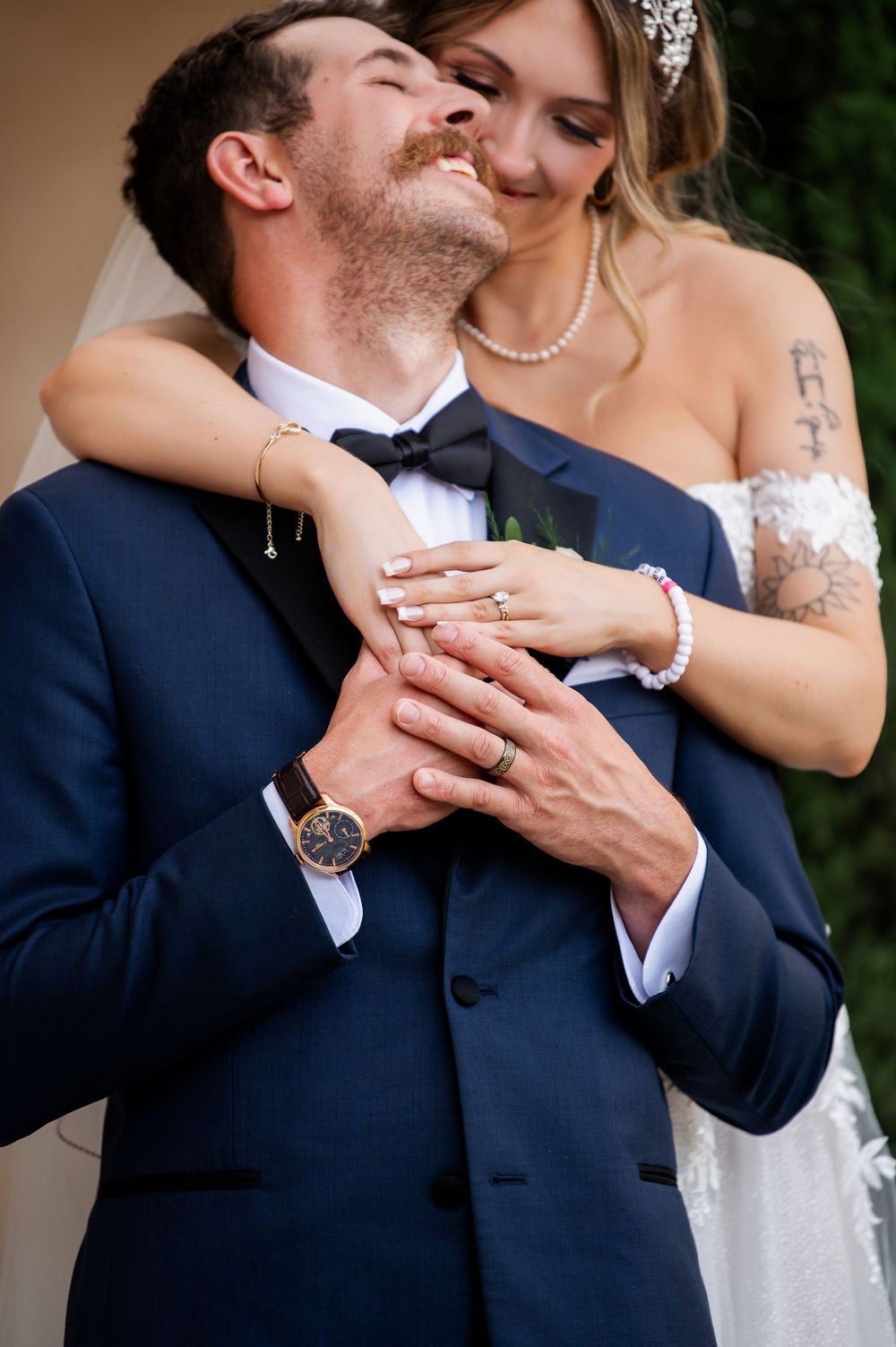 A close-up wedding photo showing hands with rings and intimate embrace.