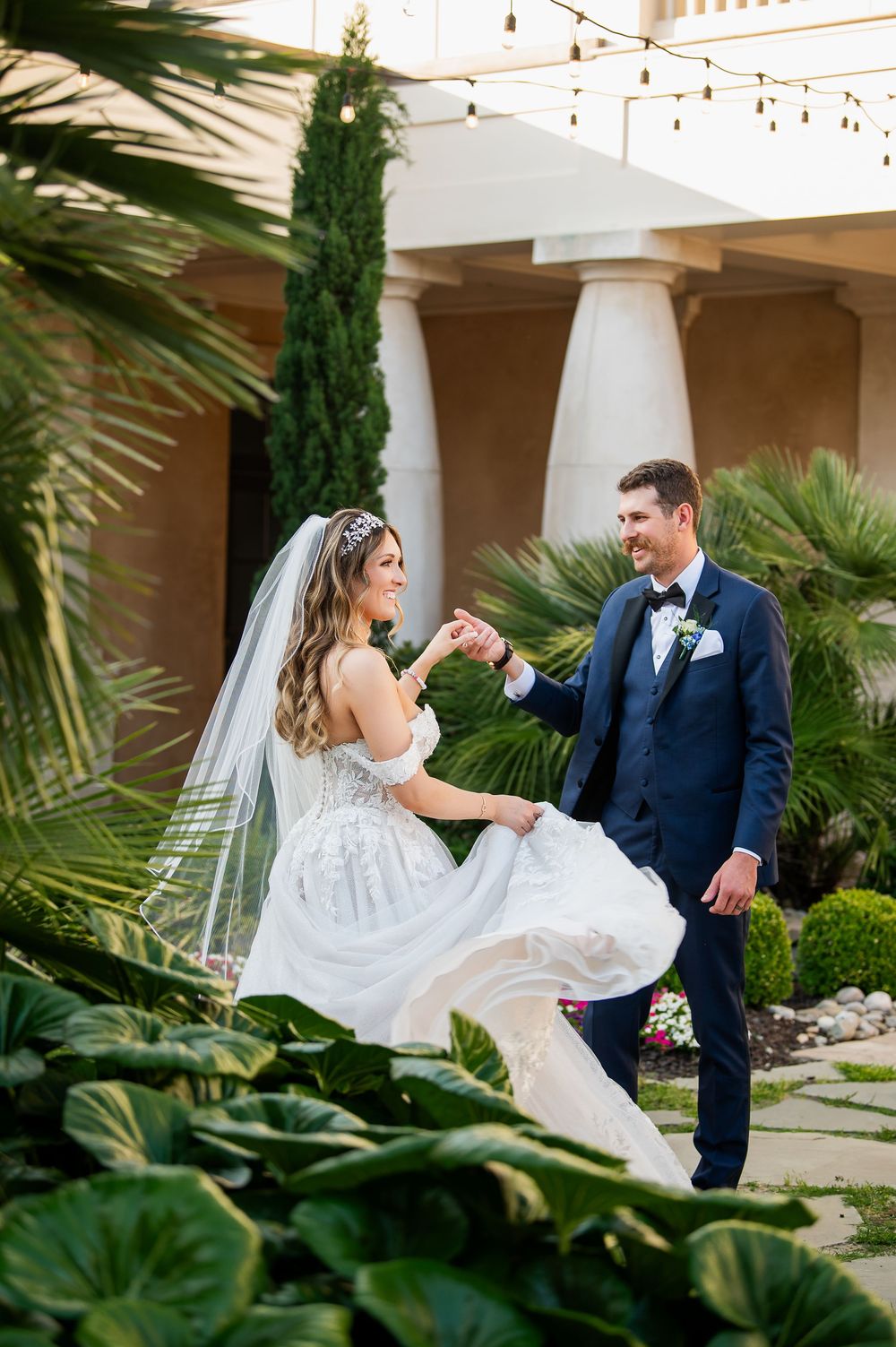 Couple dances in garden setting with bride's dress twirling among tropical plants.
