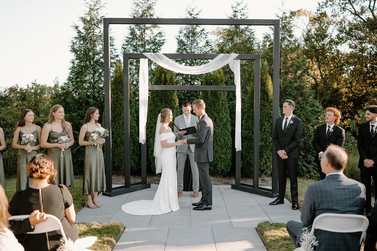 Outdoor wedding ceremony at Osage House during sunset with guests gathered on a patio surrounded by lush greenery.