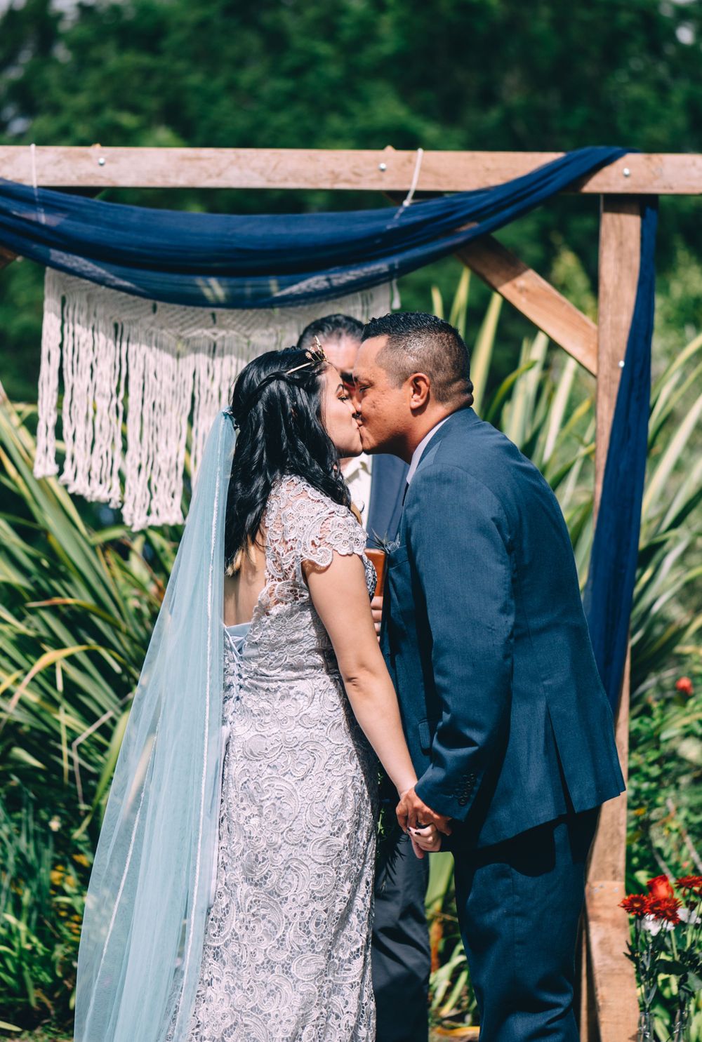 A couple shares a tender moment during their outdoor wedding ceremony beneath a decorated wooden arch.