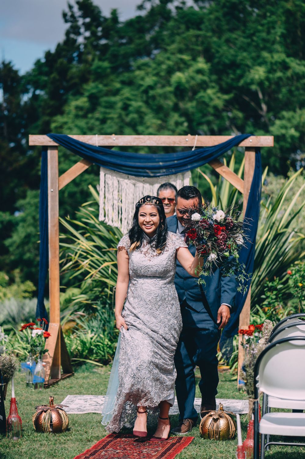 An outdoor wedding ceremony setup with wooden posts, blue draping, and natural garden surroundings.