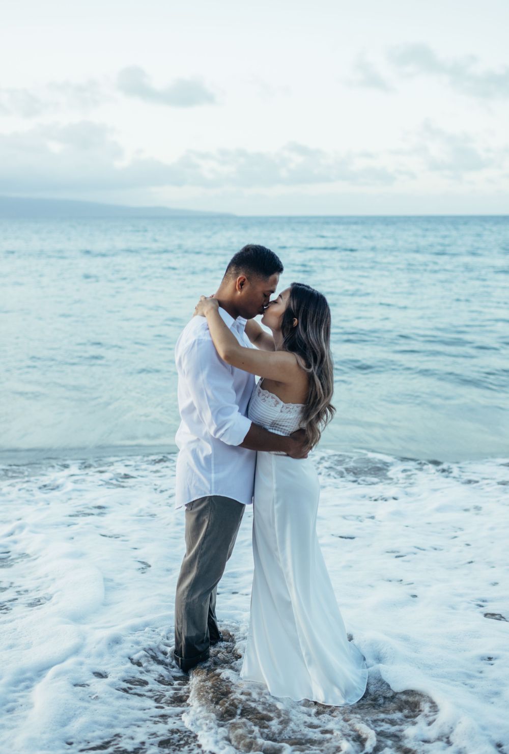 A couple shares an intimate moment as ocean waves splash around them.